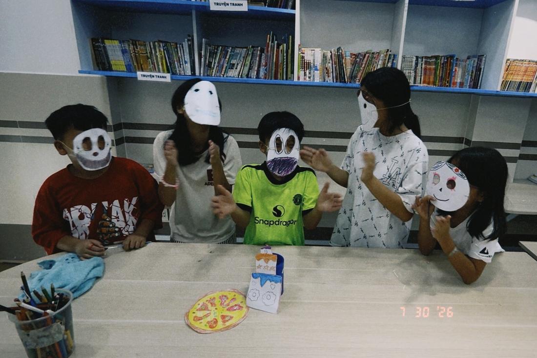 Children holding up paper masks they drew and cut out in the art class.