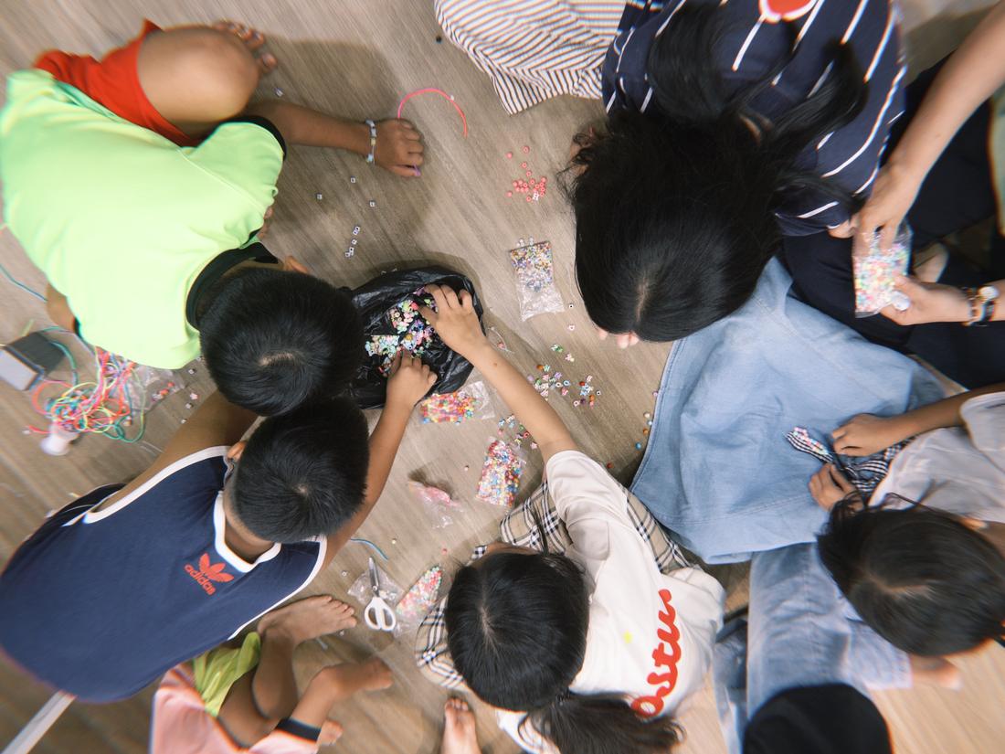 Overhead photo of children sitting in a circle threading colourful beads into bracelets.